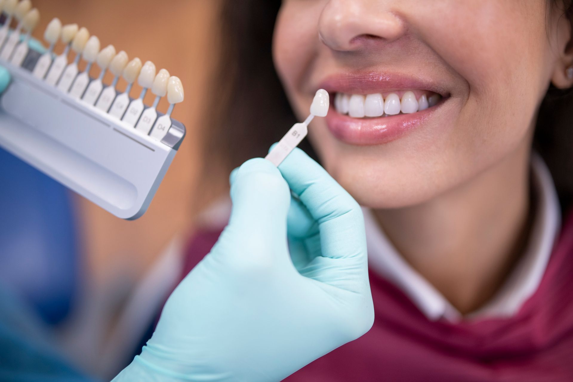 A dentist using a palette tooth color sample close to the patient's teeth for cosmetic dentistry.