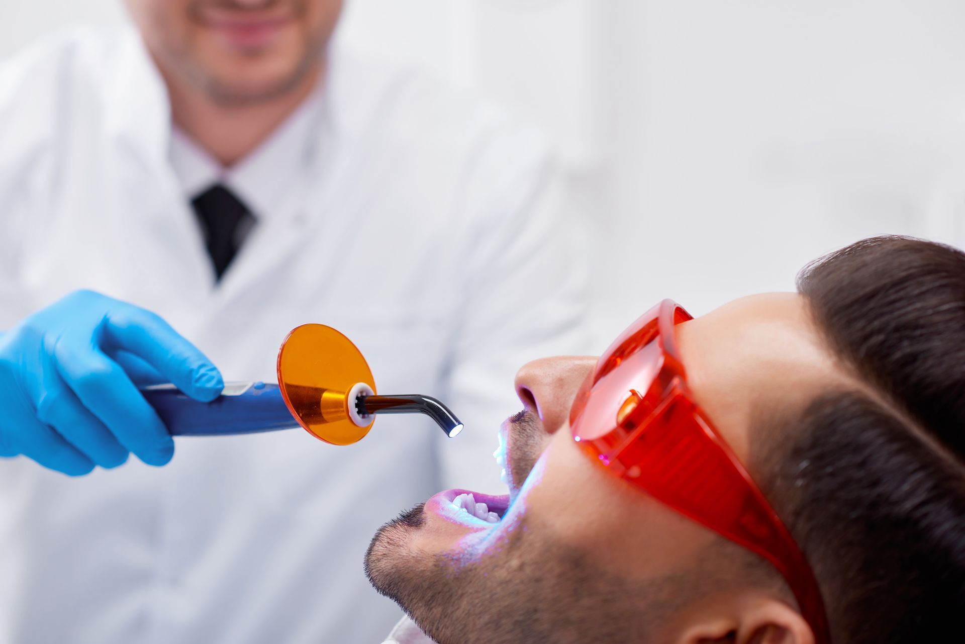 Dentist using curing light device during professional dental treatment in a modern clinic setting.