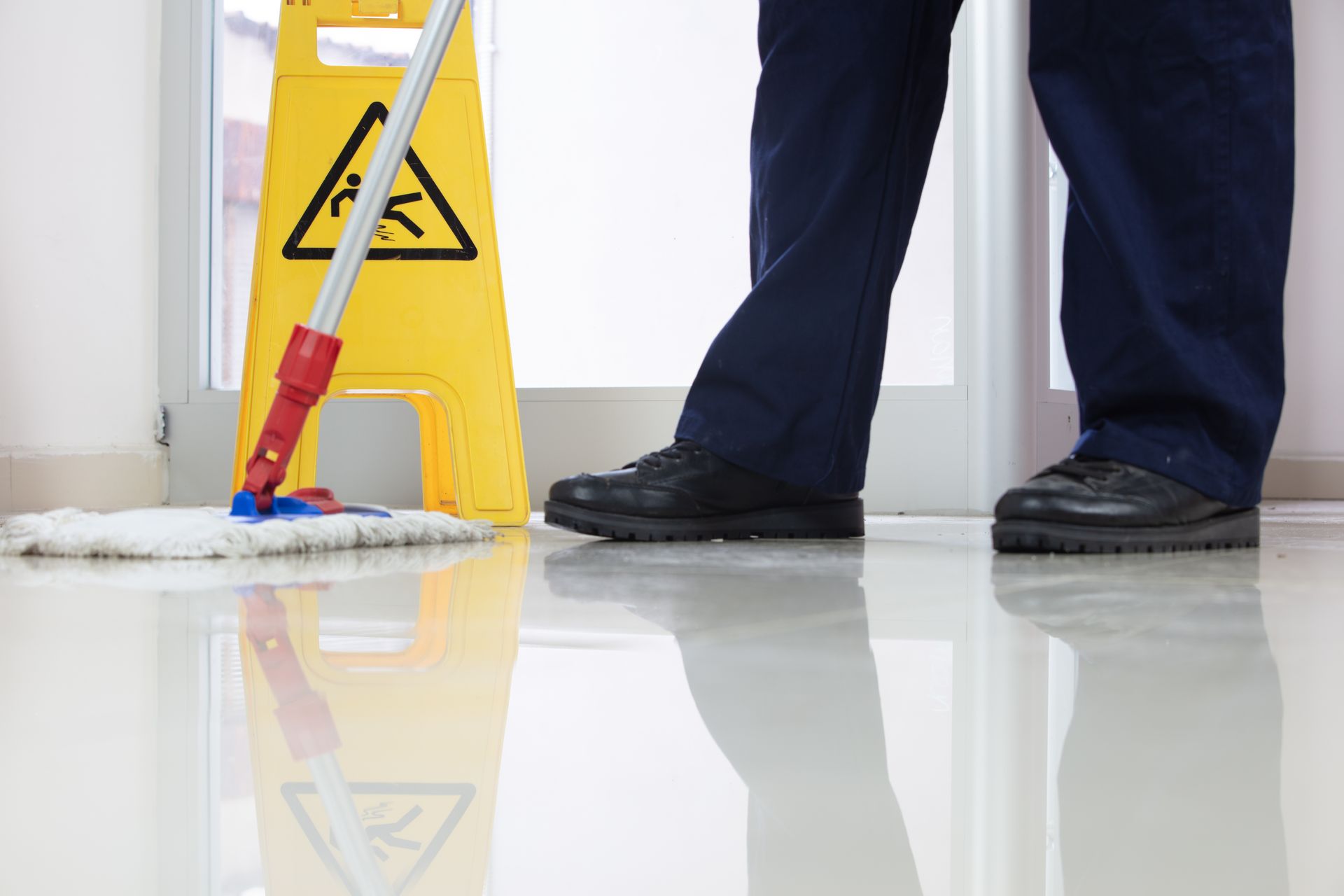 A man is mopping the floor next to a yellow caution sign.