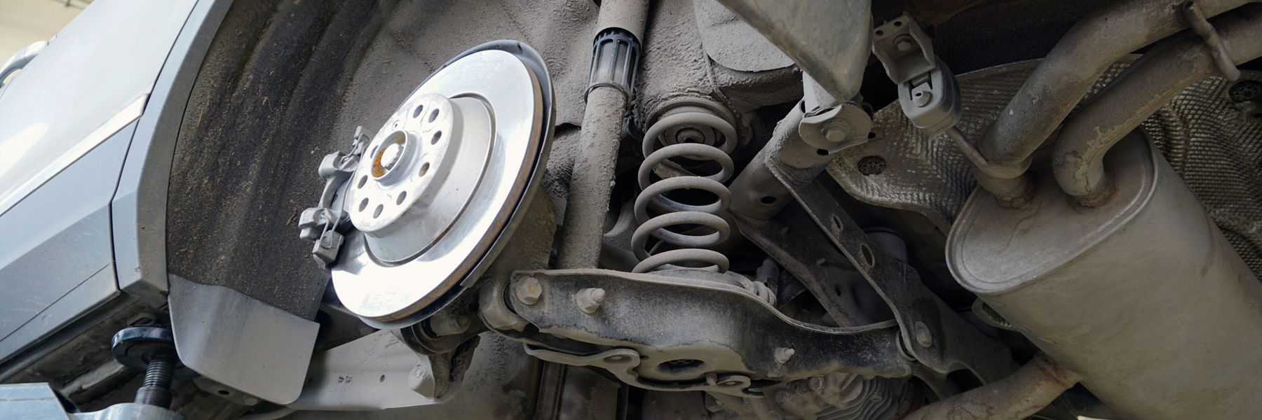 Close-up of a car’s front wheel, brake disc, and suspension components underneath the vehicle
