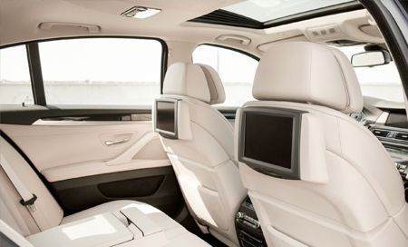 Interior view of a car's back seats with beige leather and screens attached to the headrests.