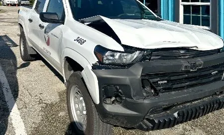 White Chevrolet pickup truck with front-end damage, parked near a building.