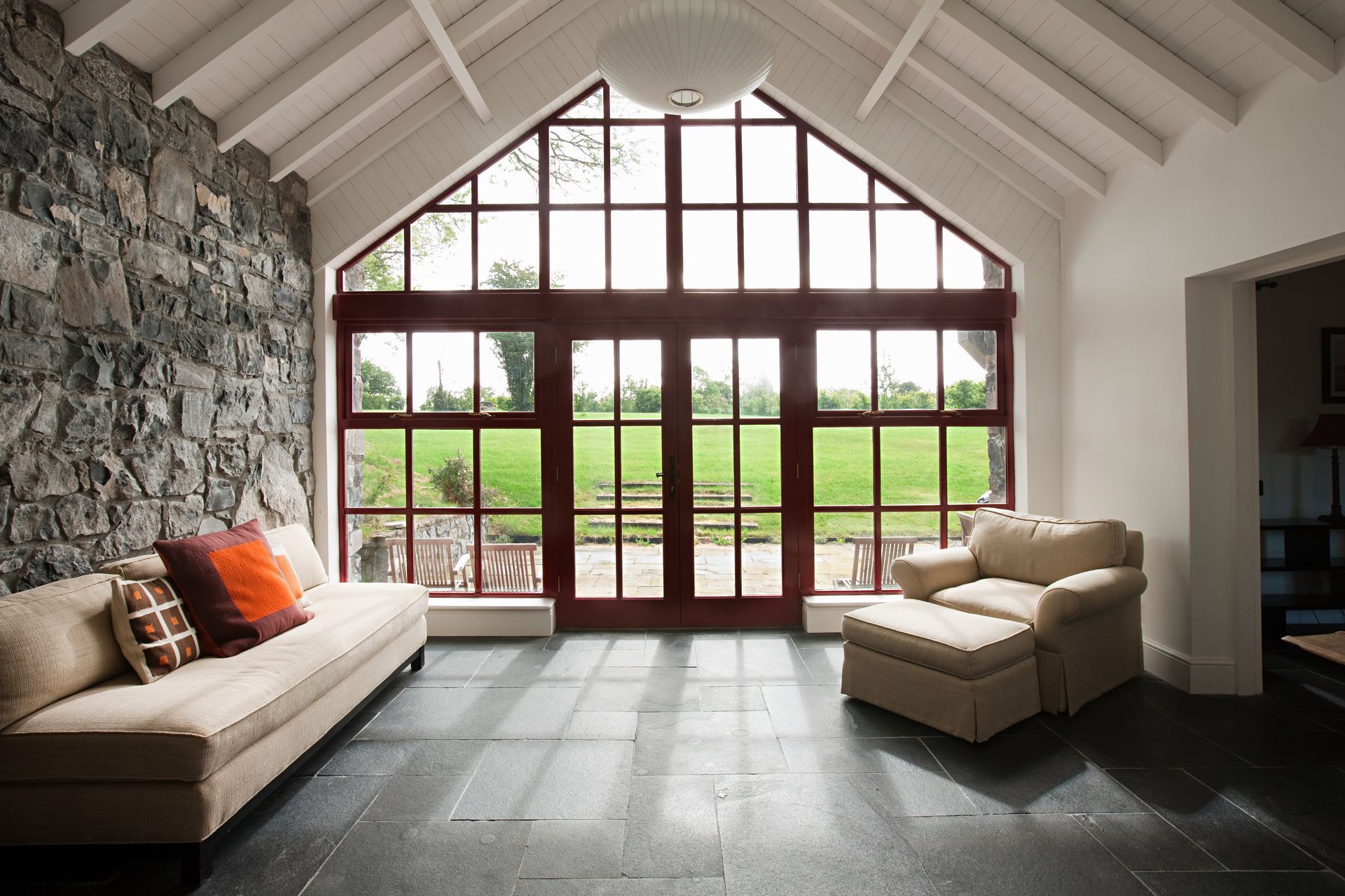 Sunroom with stone wall, large windows overlooking a grassy yard, and a sofa and armchair.
