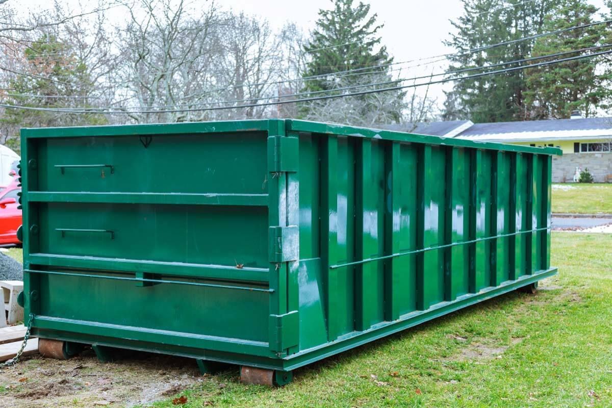 Green dumpster on grass, likely for waste disposal, in a residential setting.