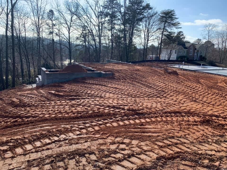 Dirt construction site with tire tracks and retaining wall, trees in background.
