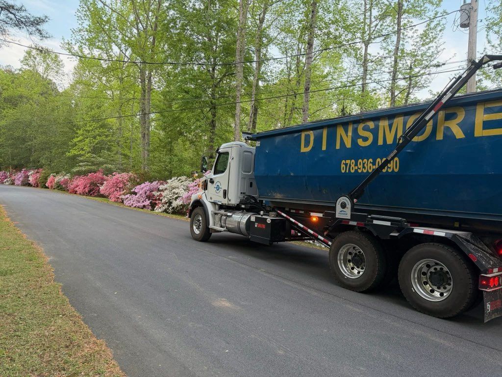 Blue Dinsmore dump truck parked on a winding road beside pink azalea bushes and trees