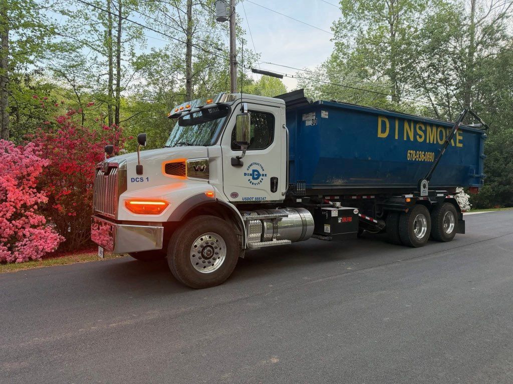 White Dinsmore dump truck parked on a road beside trees and red bushes