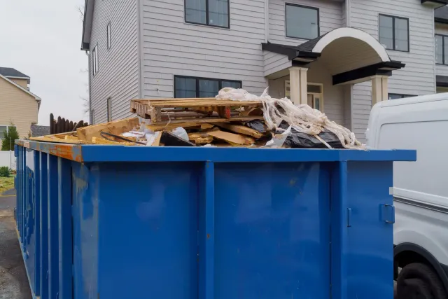 Blue dumpster filled with construction debris in front of a house.