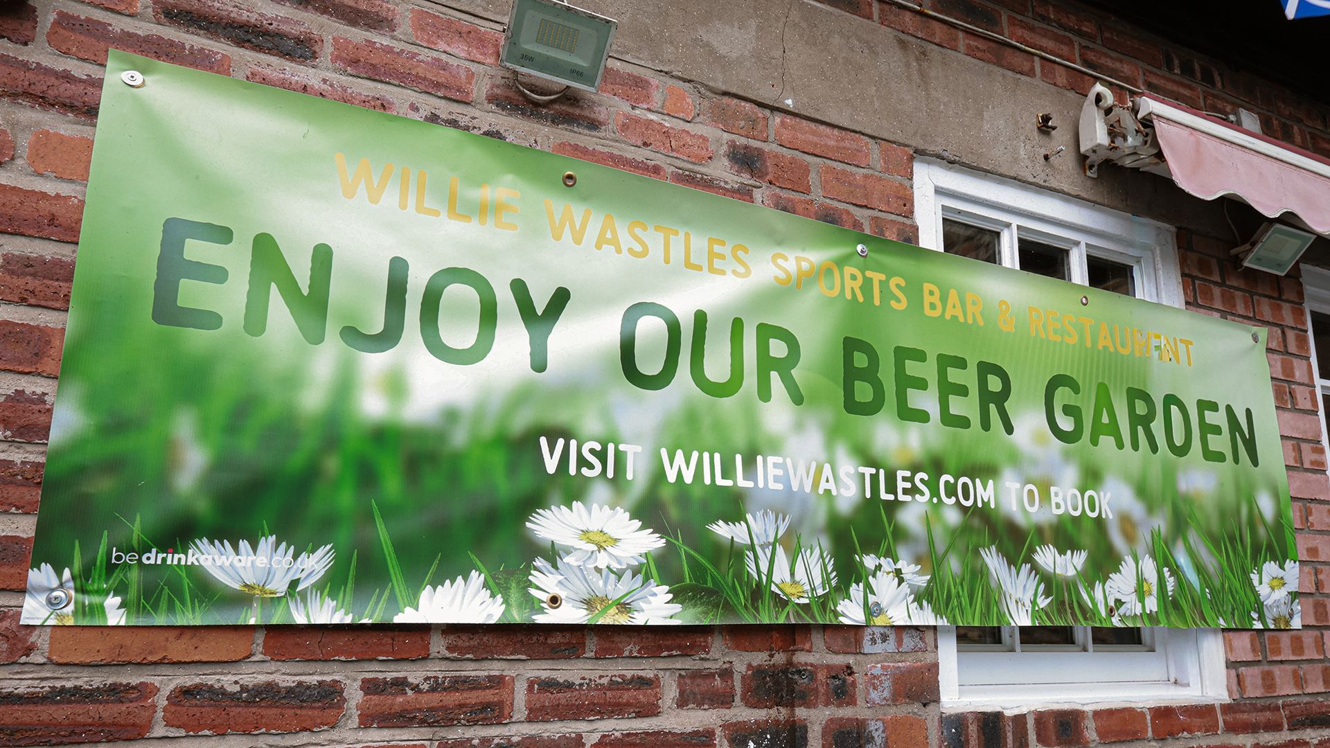 Green banner on brick wall reads “ENJOY OUR BEER GARDEN” at Willie Wastle’s Sports Bar.