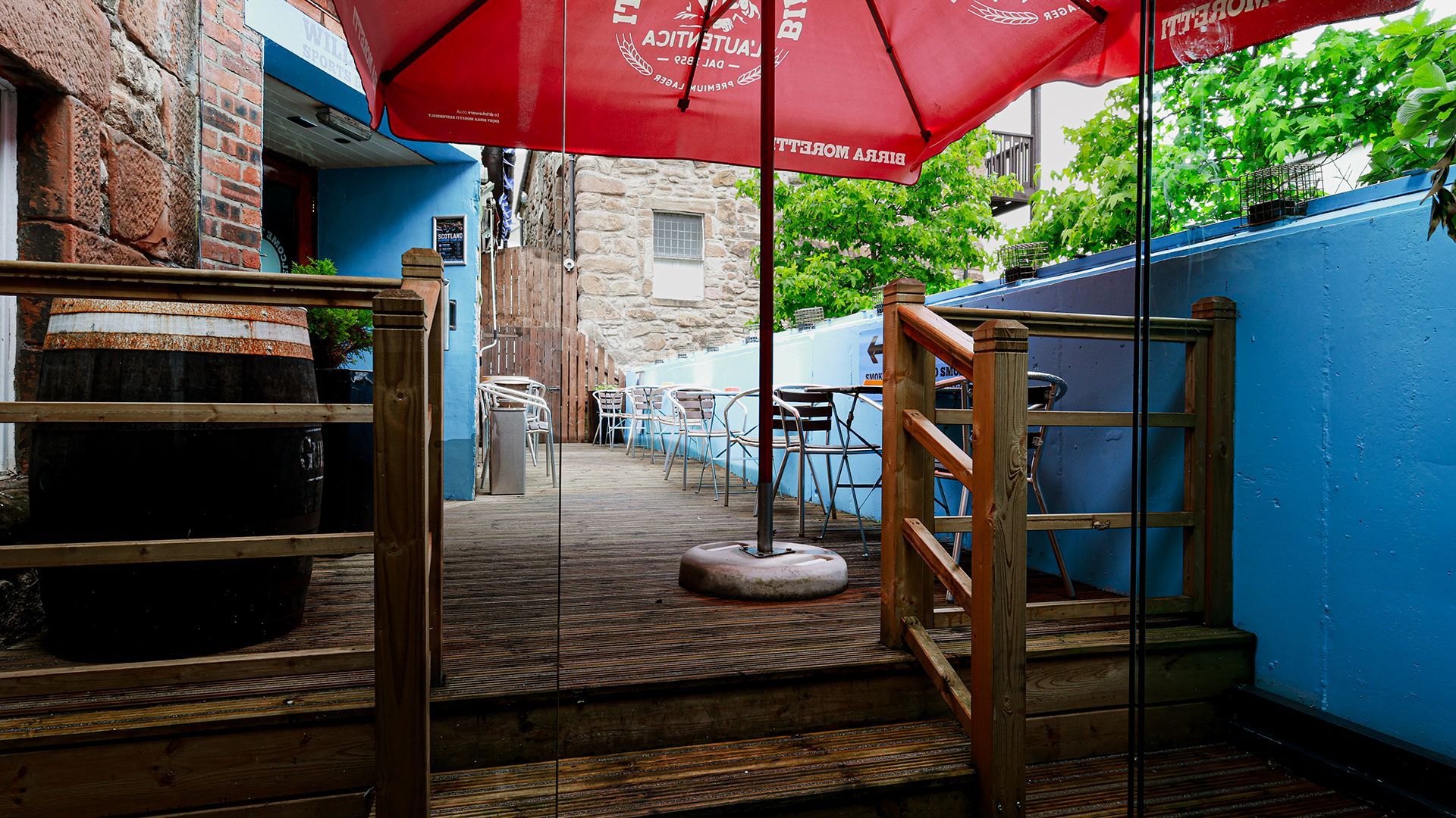 Outdoor patio with wooden deck, red umbrella, blue wall, and a small table between railings.