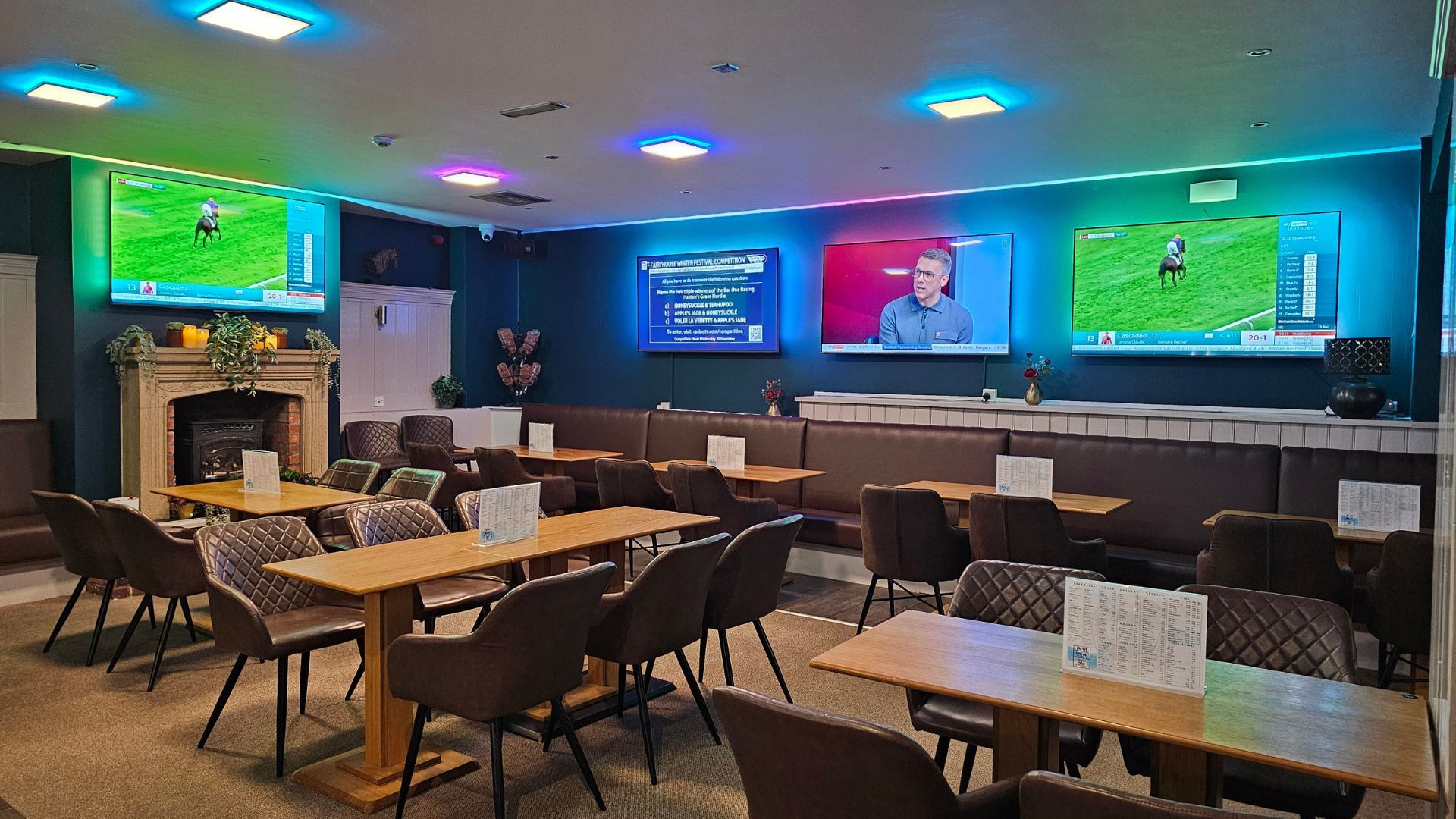 Sports bar dining area with TVs showing a game, tables and chairs, and a lit fireplace on the left