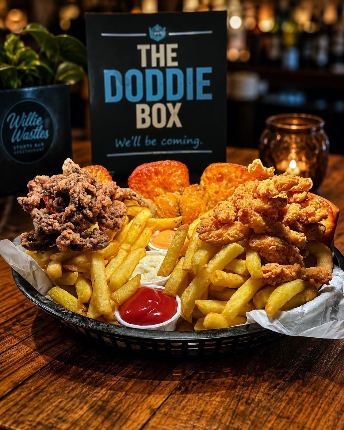 Loaded fries with fried chicken and ketchup on a table, with a sign reading “The Doddie Box” behind it.