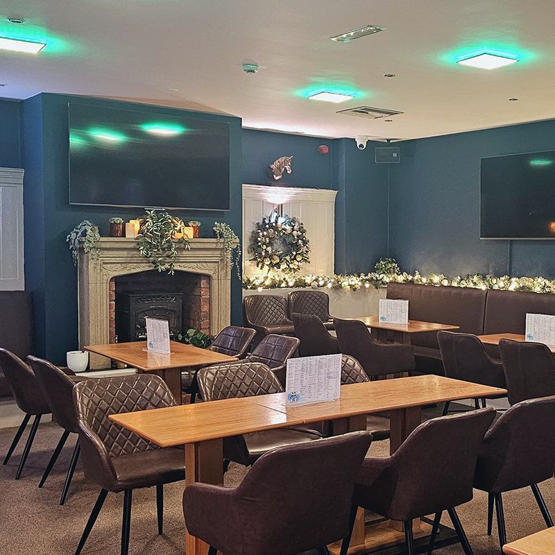 Cozy lounge with brown chairs and tables, blue walls, fireplace, wreath, and soft green accent lighting.