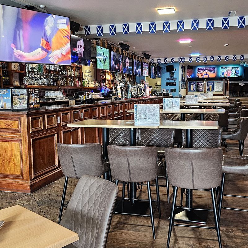 Empty sports bar interior with TVs, wooden bar, and rows of stools and tables.