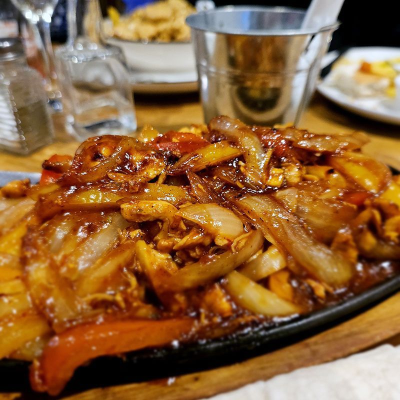 Glazed stir-fried noodles with onions and peppers on a black serving plate at a restaurant table