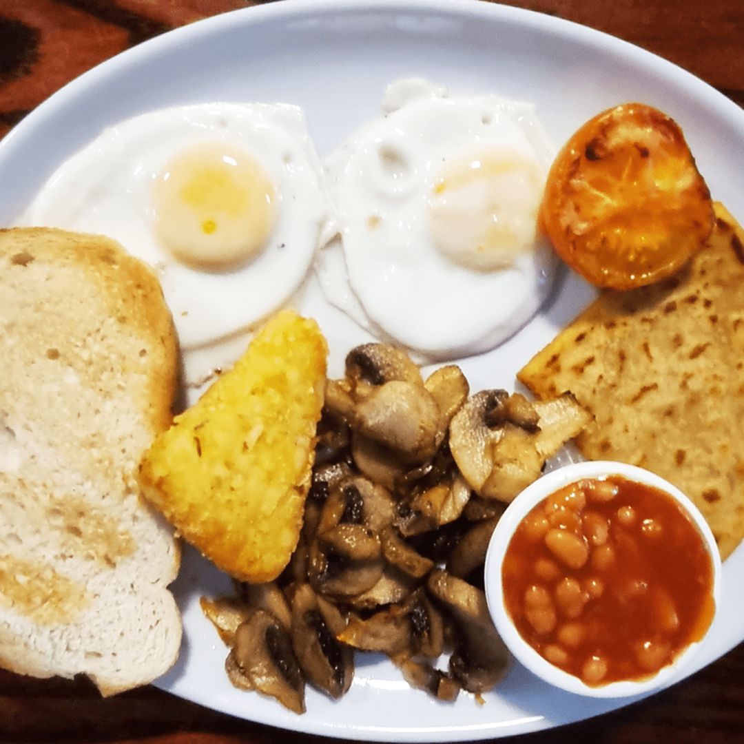 Breakfast plate with toast, two fried eggs, hash browns, mushrooms, baked beans, and another slice of toast