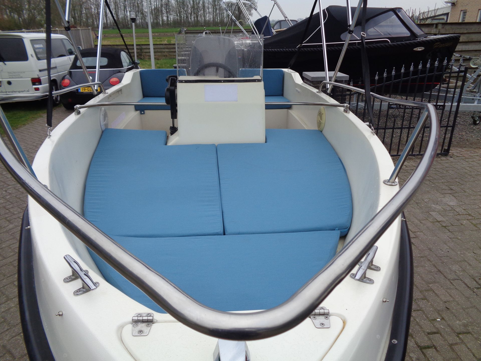 Kleine witte boot met blauwe kussens, aangemeerd in een jachthaven, gezien vanaf de boeg.