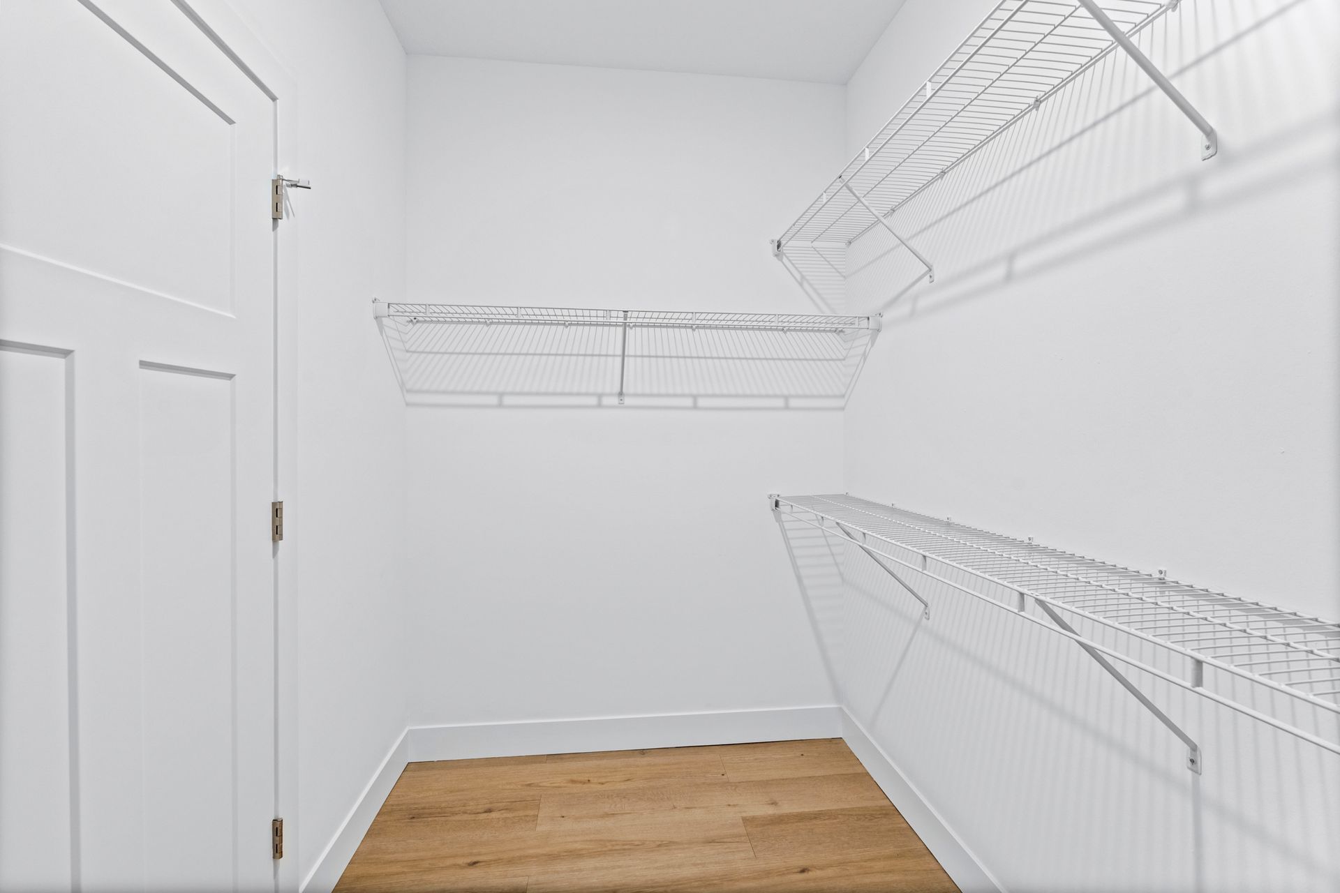 Empty white closet with wire shelves and a wooden floor.