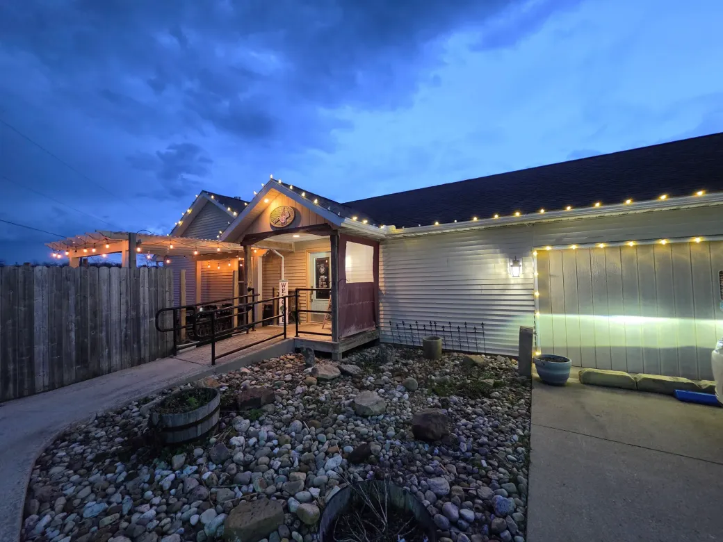 Snowy house exterior at dusk with warm porch lights and a lit garage walkway