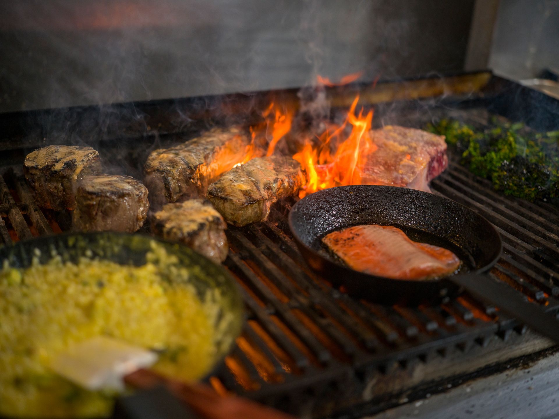 Grill with steaks and vegetables cooking over open flames in a barbecue pit