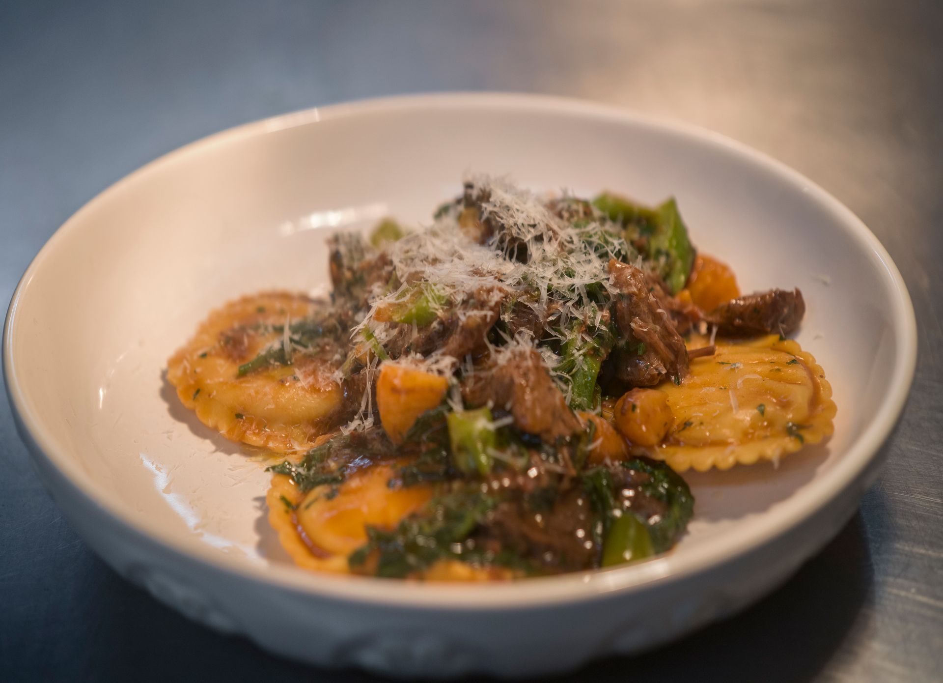 Plated ravioli topped with herbs and grated cheese in a white bowl, served on a table