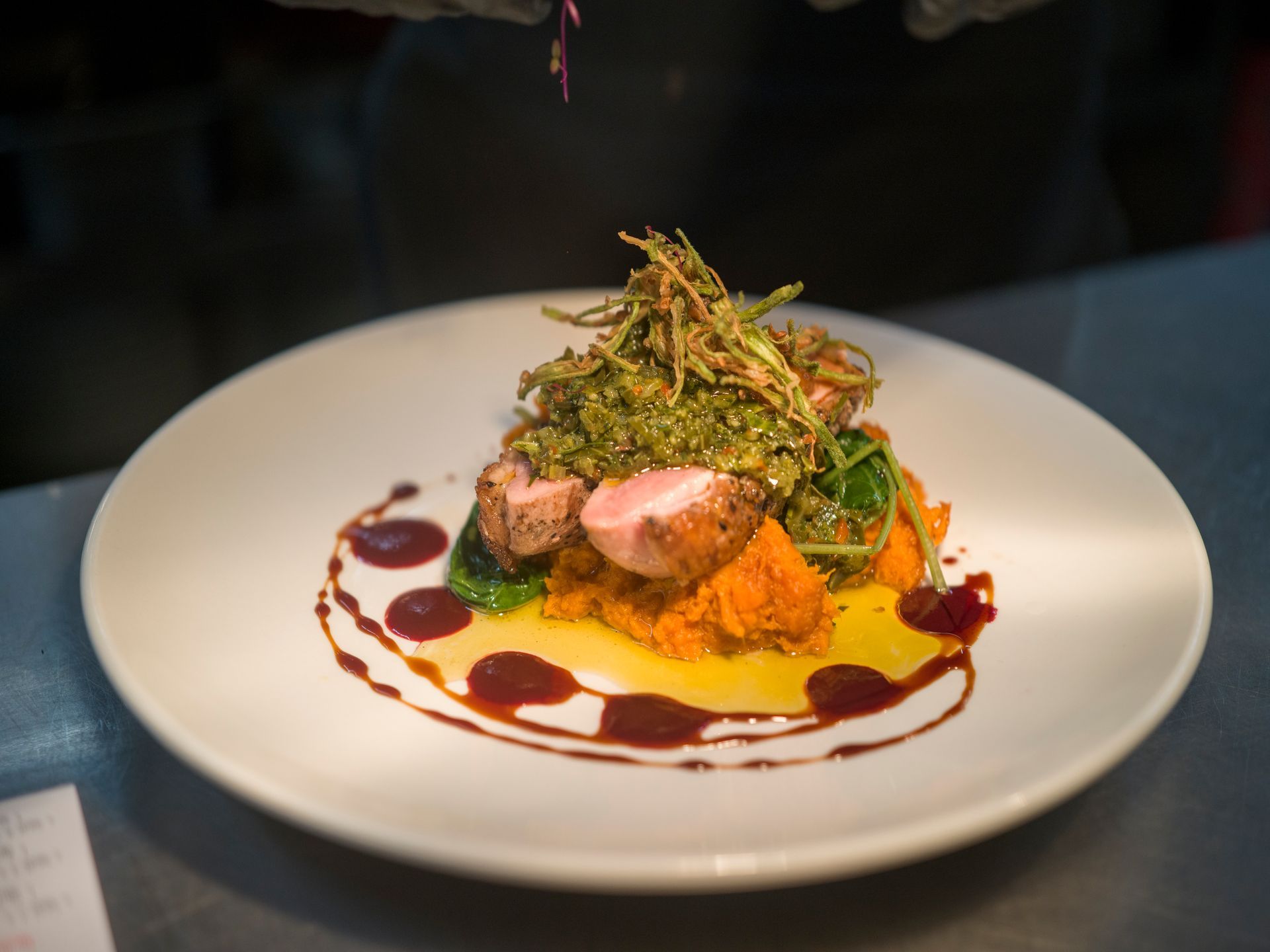Plated gourmet dish with sliced meat, greens, and sauce on a white plate