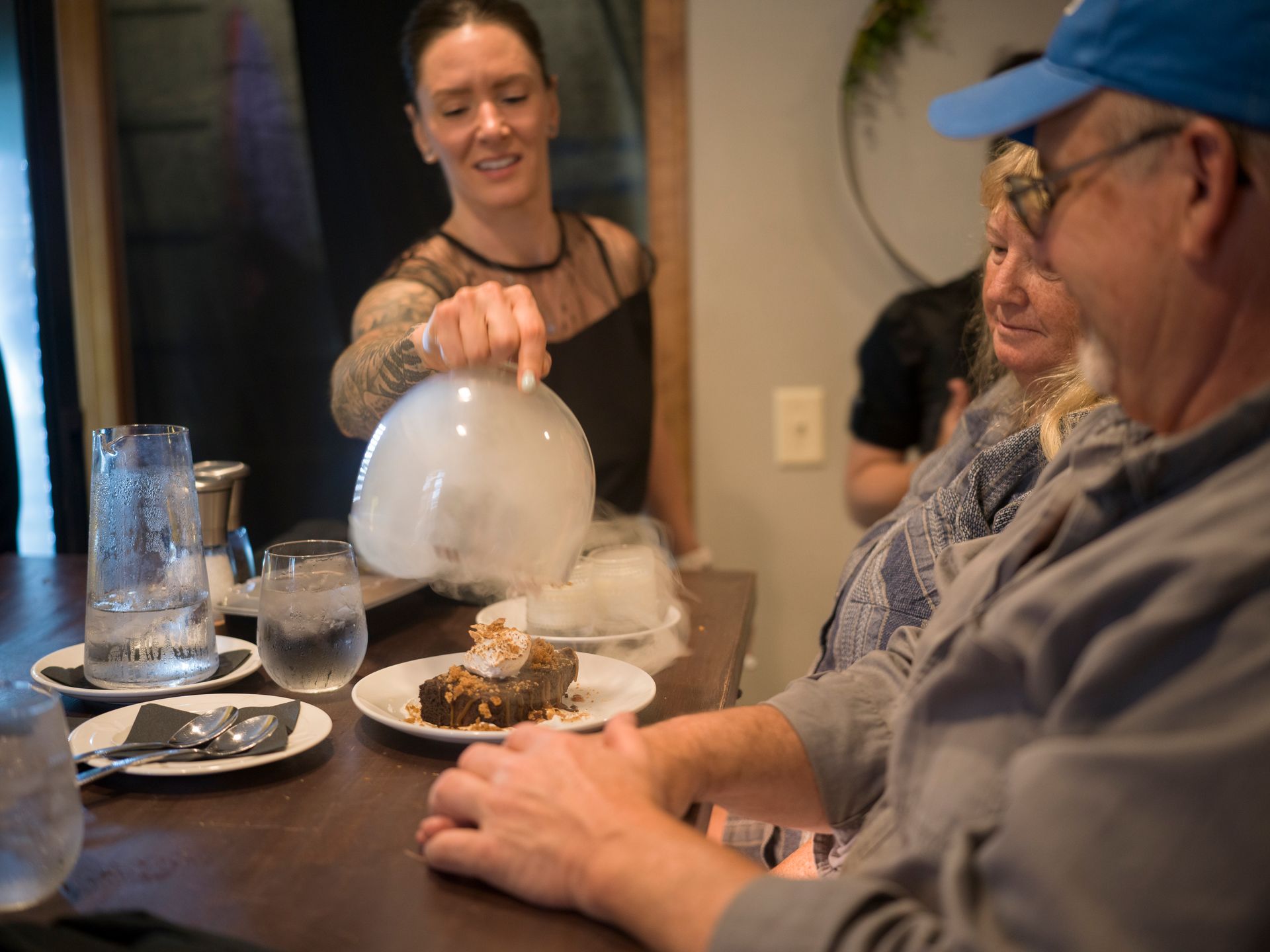 Woman serving dry ice smoke to diners at a table in a restaurant