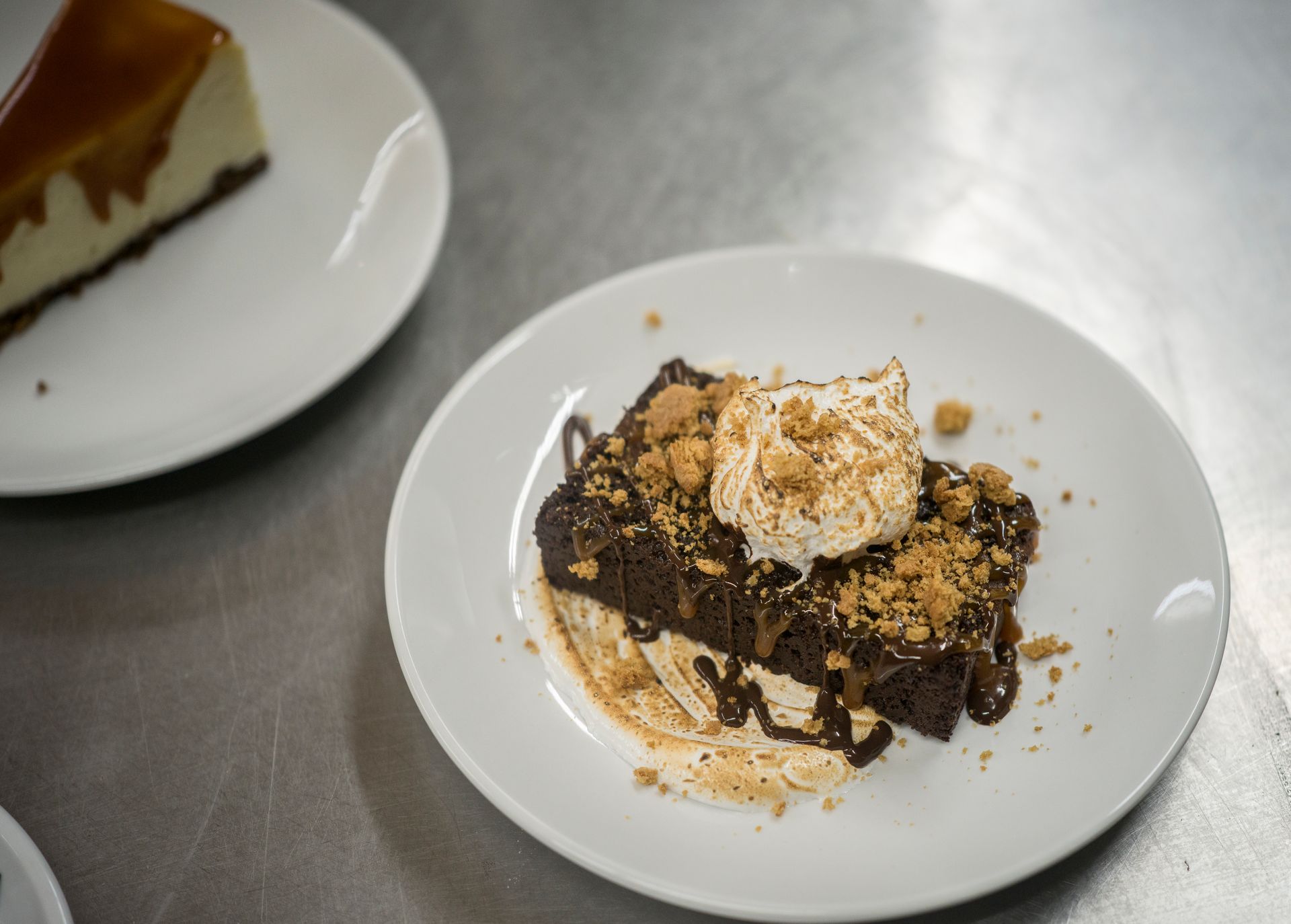 Dessert on a white plate topped with whipped cream and chocolate drizzle on a metal table