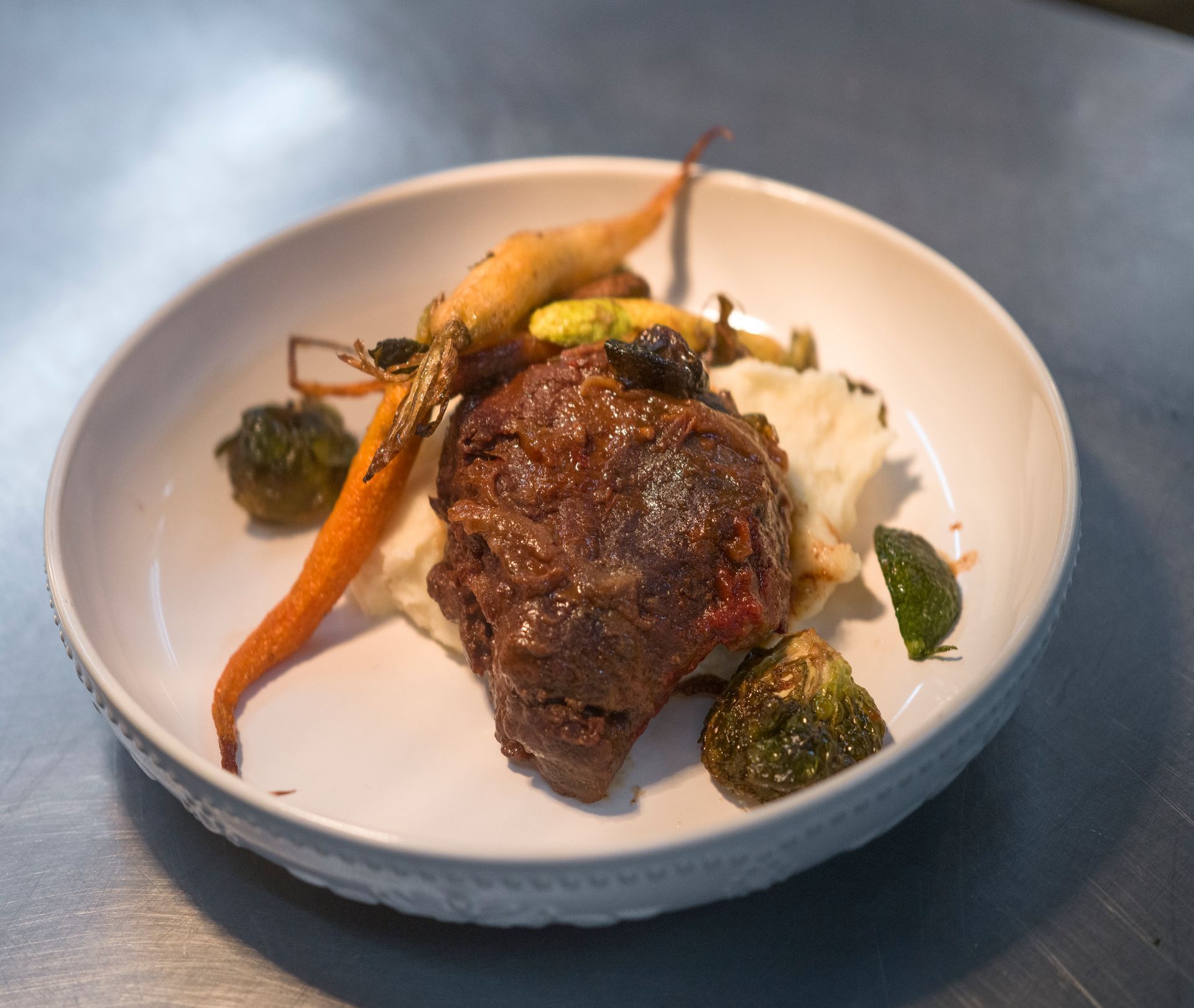 Plated gourmet dish with seared meat, roasted vegetables, and mashed potatoes on a white plate