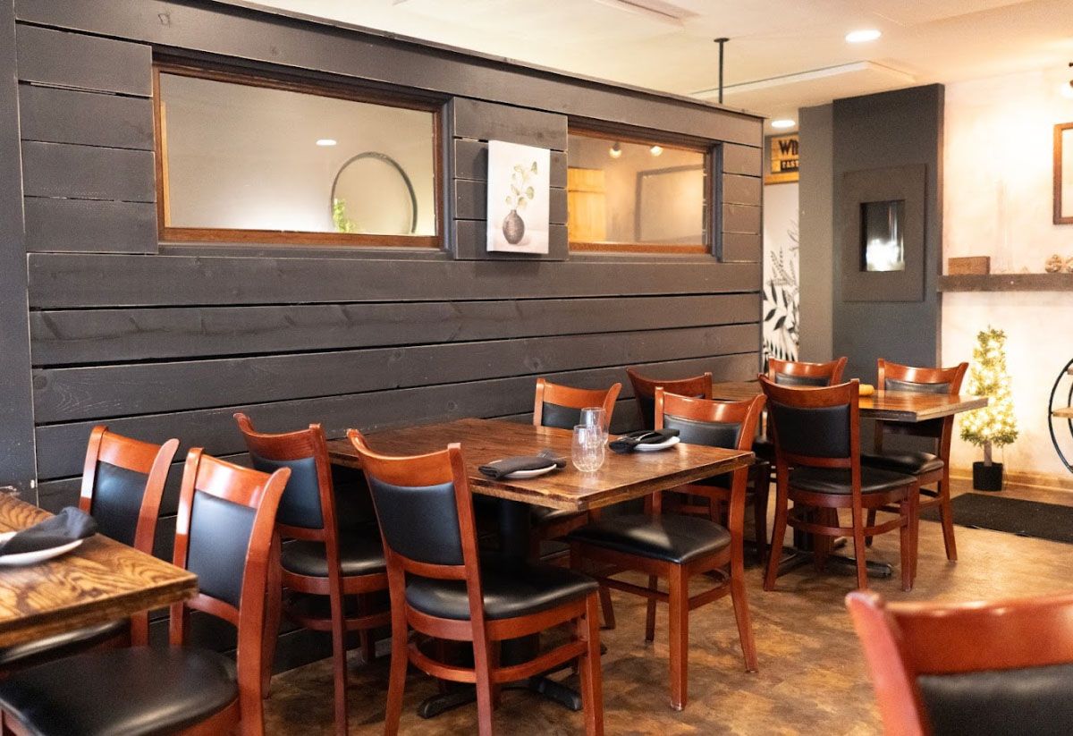 Warm restaurant dining area with wooden tables and chairs, dark accent wall, and soft ambient lighting.