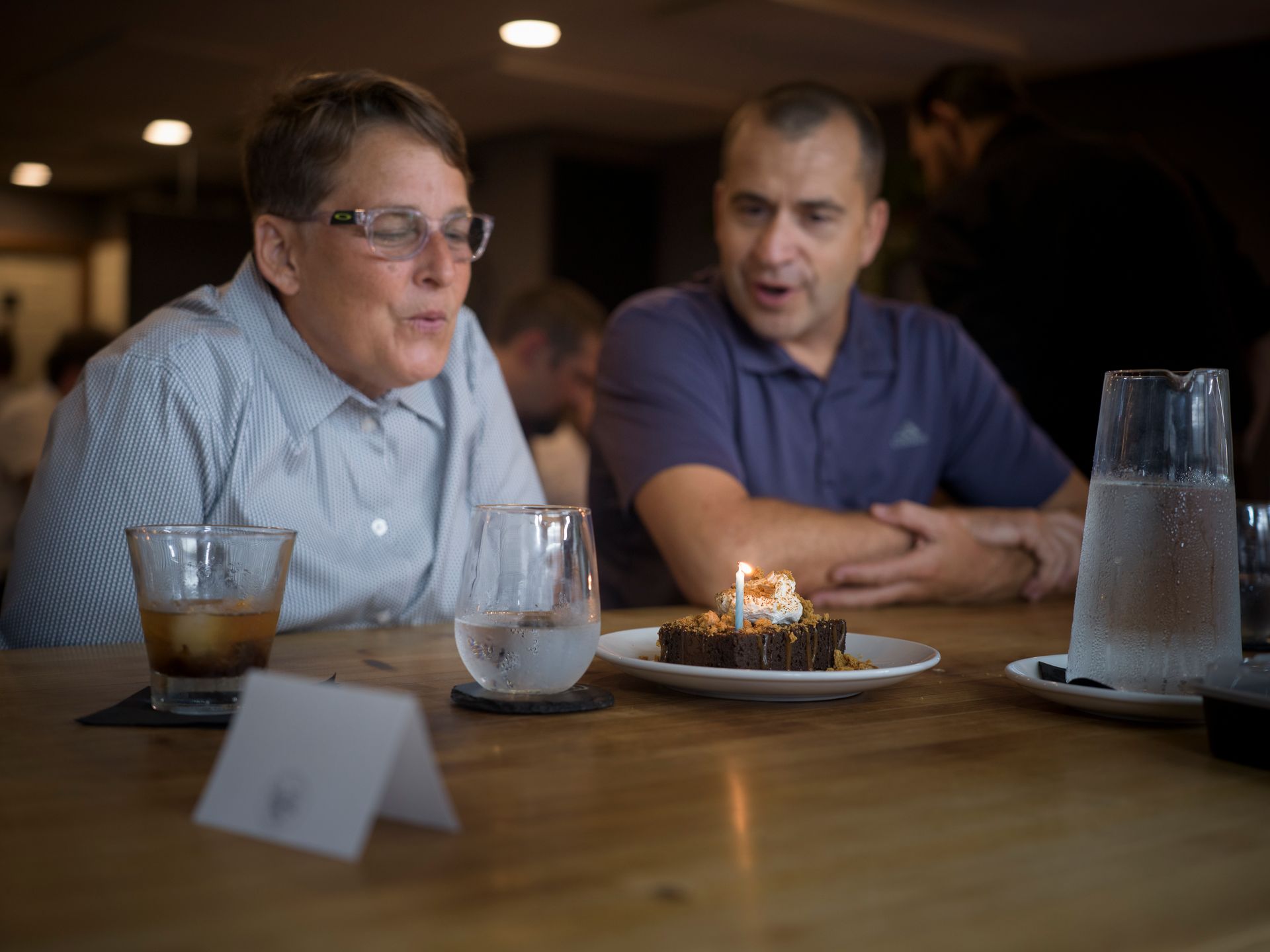 Two people talking at a restaurant table with drinks and a dessert candle in the center