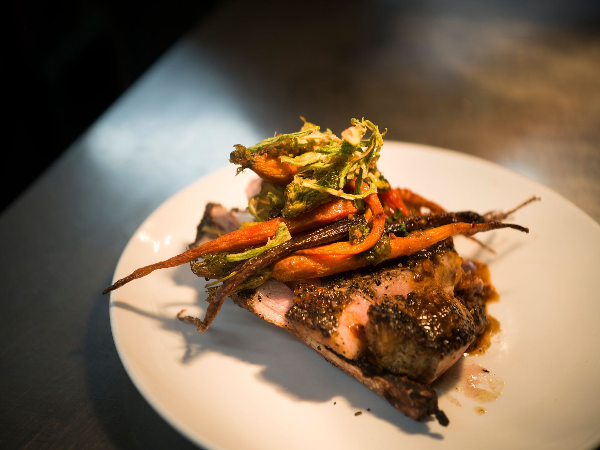 Plated seared fish topped with vegetables on a white dish in a dimly lit restaurant setting
