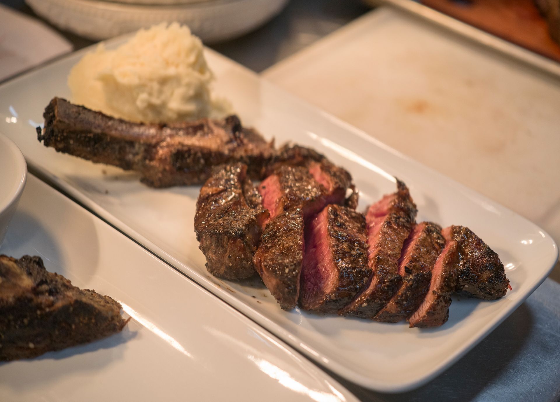 Sliced grilled steak on a white plate with mashed potatoes and a side of sauce