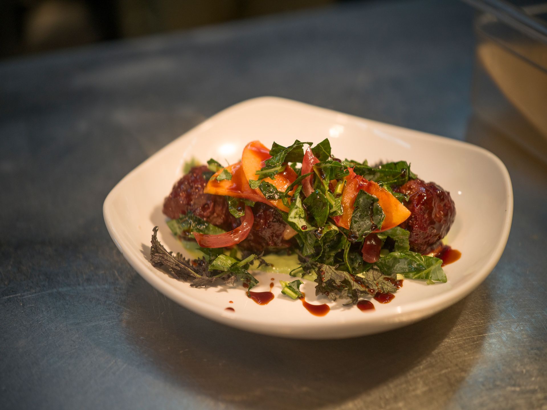 Plated dish of meatballs topped with greens and red pepper on a white bowl