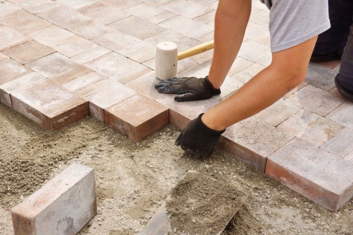 Worker laying beige pavers on a sand base for a patio walkway