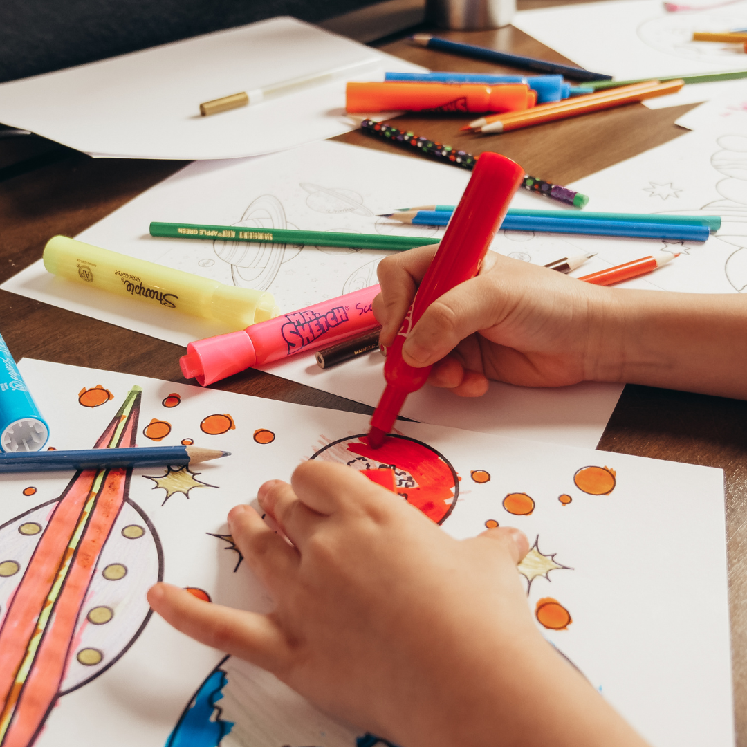 A child is drawing a rocket with a red marker