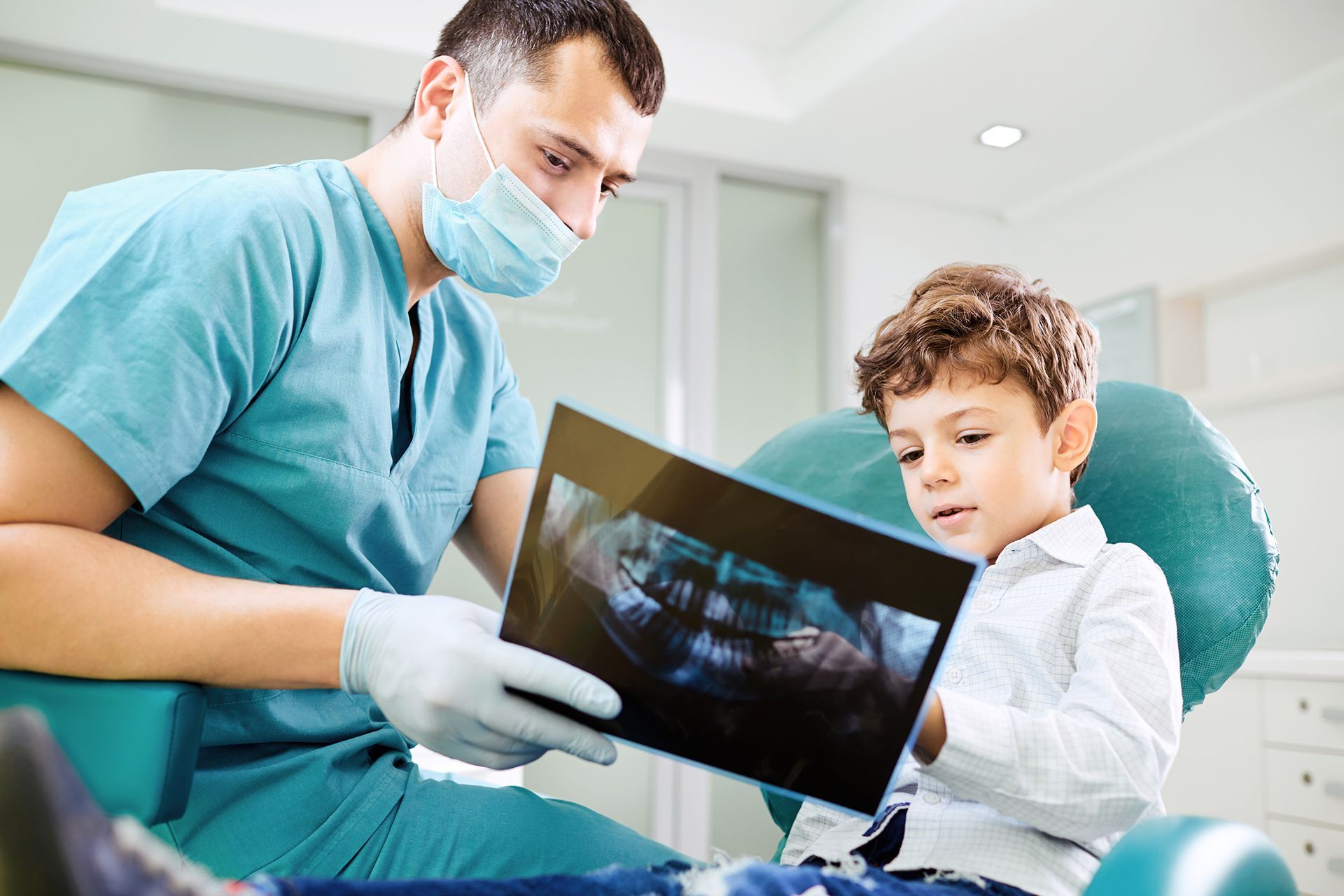 A boy and a dentist look at an x-ray image of teeth.