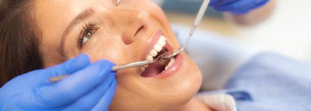 Woman at the dentist, smiling. Dental tools in mouth, blue-gloved hands, close-up.