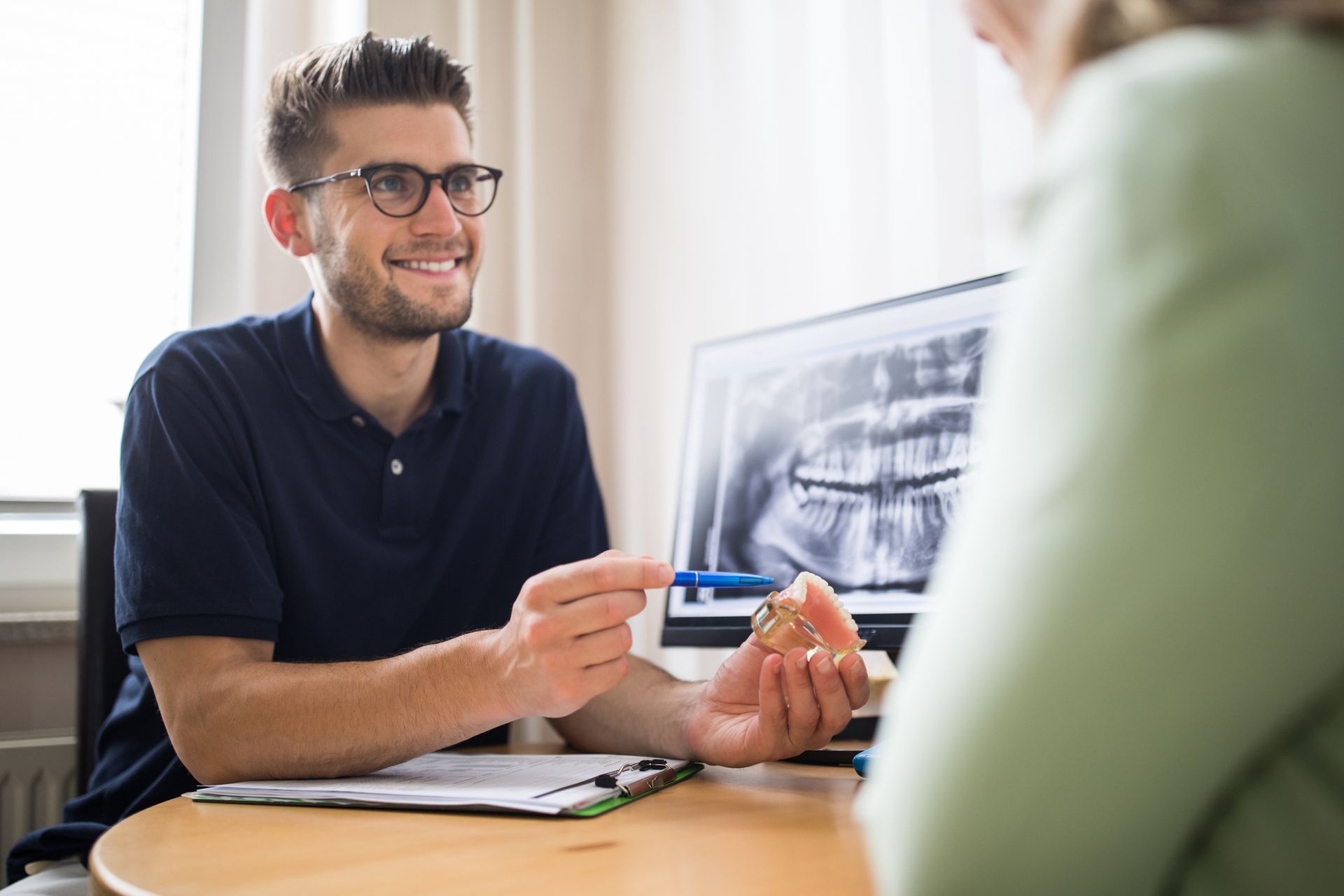 A man is sitting at a table talking to a woman while holding a model of a tooth.