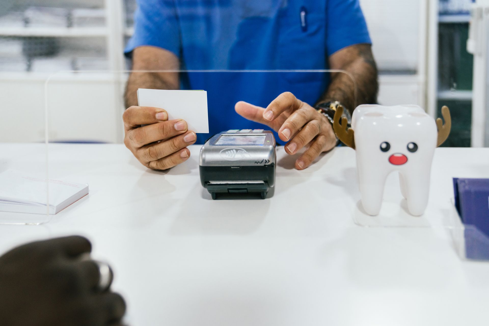 A dentist is sitting at a desk holding a card and a credit card.