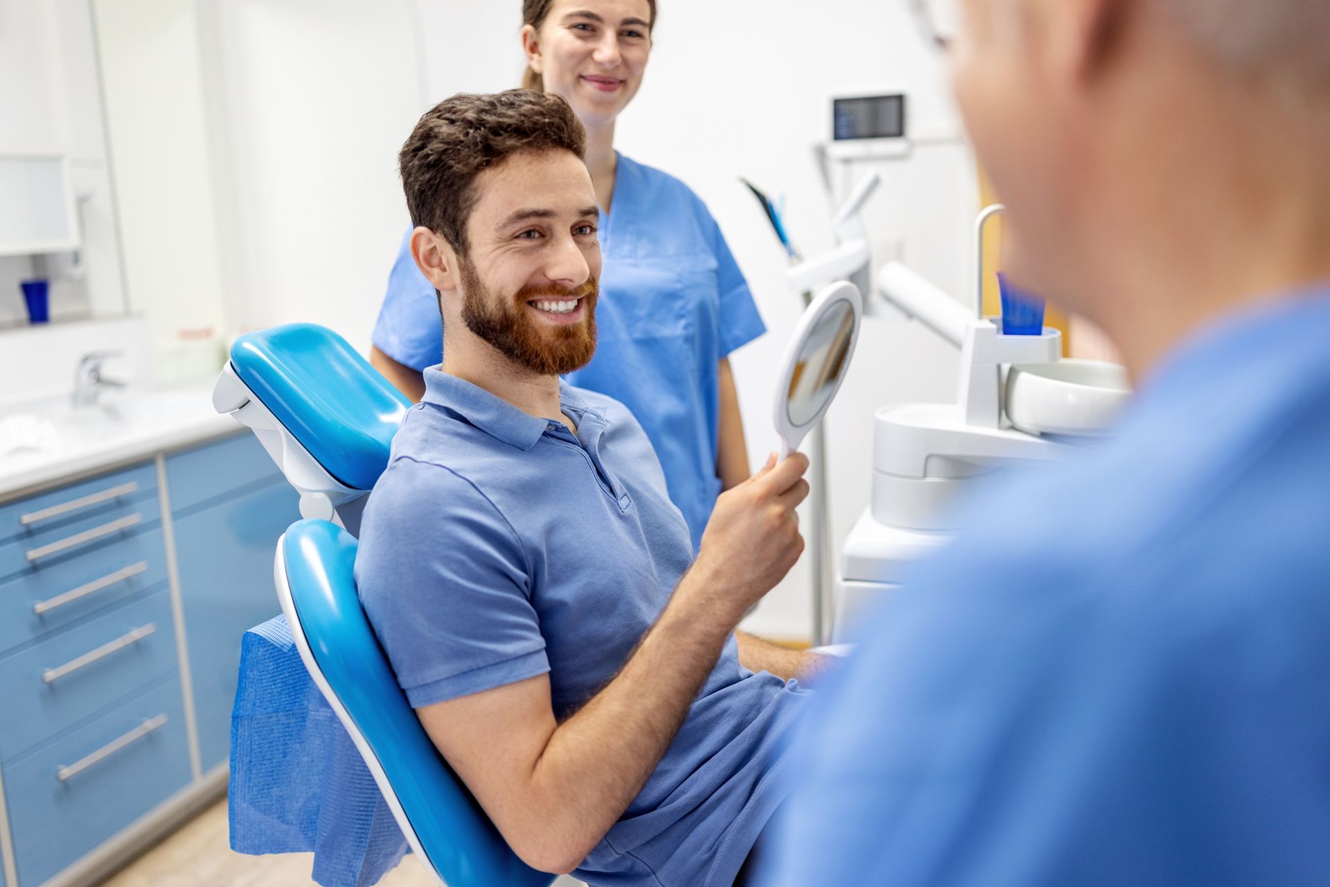 A man is sitting in a dental chair looking at his teeth in a mirror.