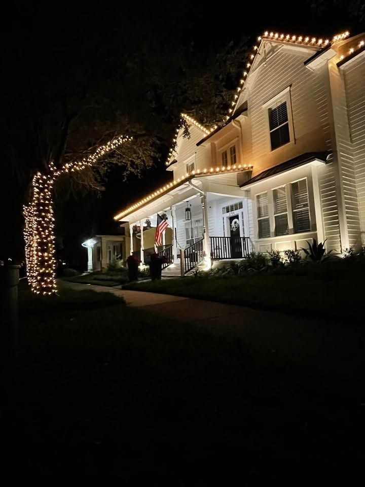 House decorated with white holiday lights at night, with a lit tree in the front yard