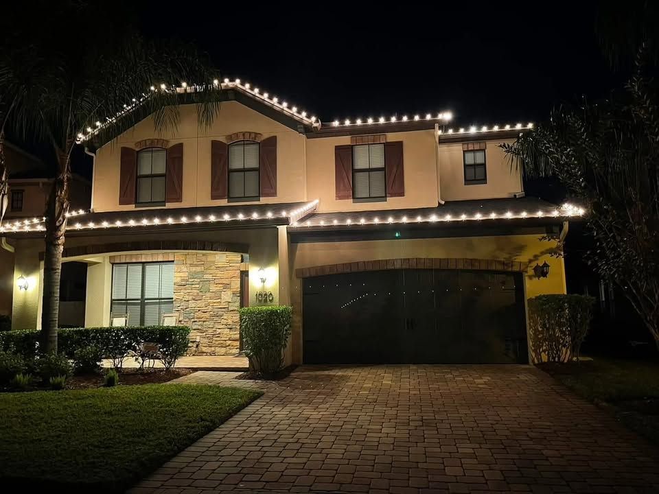 Two-story house at night with holiday lights along the roof and a lit driveway garage.