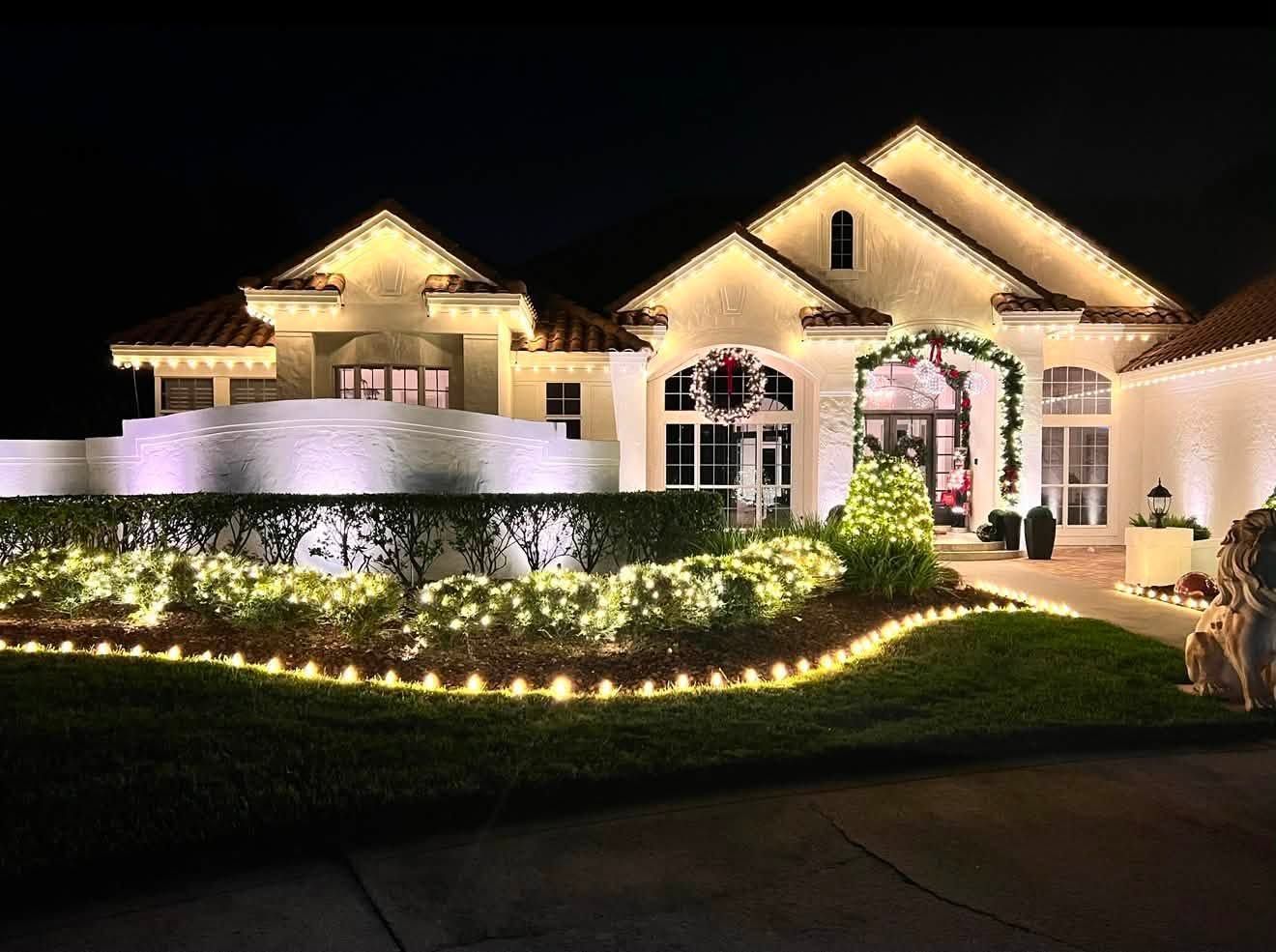 Brightly lit suburban house at night with landscaped lawn and holiday lights wrapping the walkway and entrance