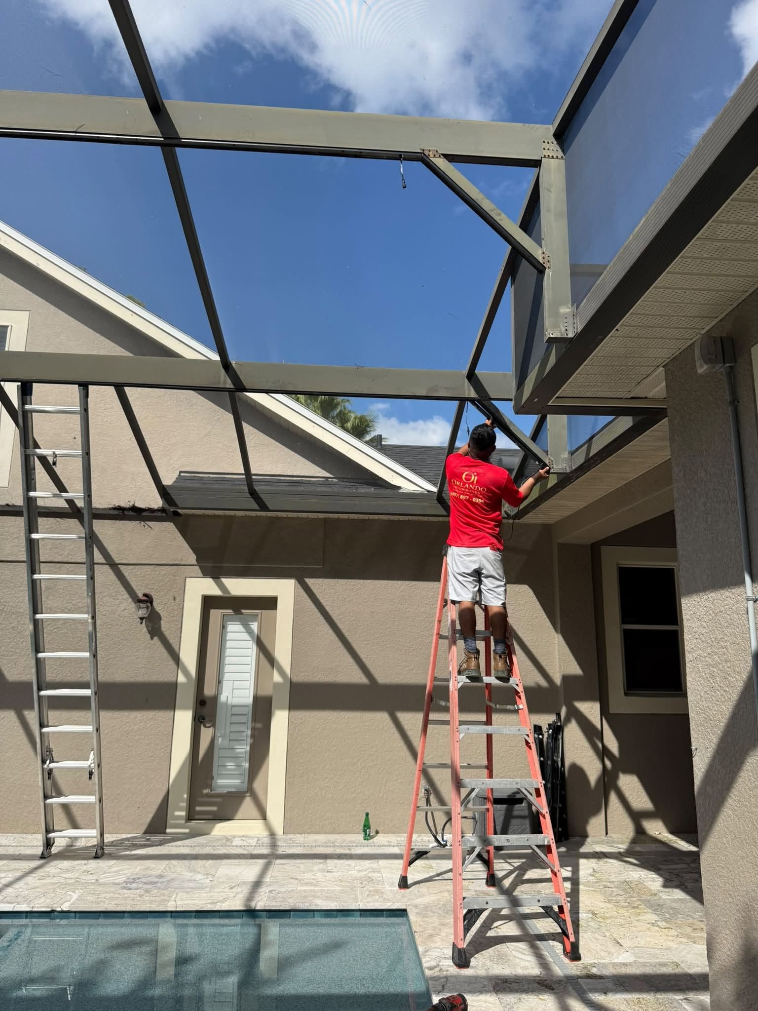Worker on ladder installing a metal pergola frame in a backyard patio.