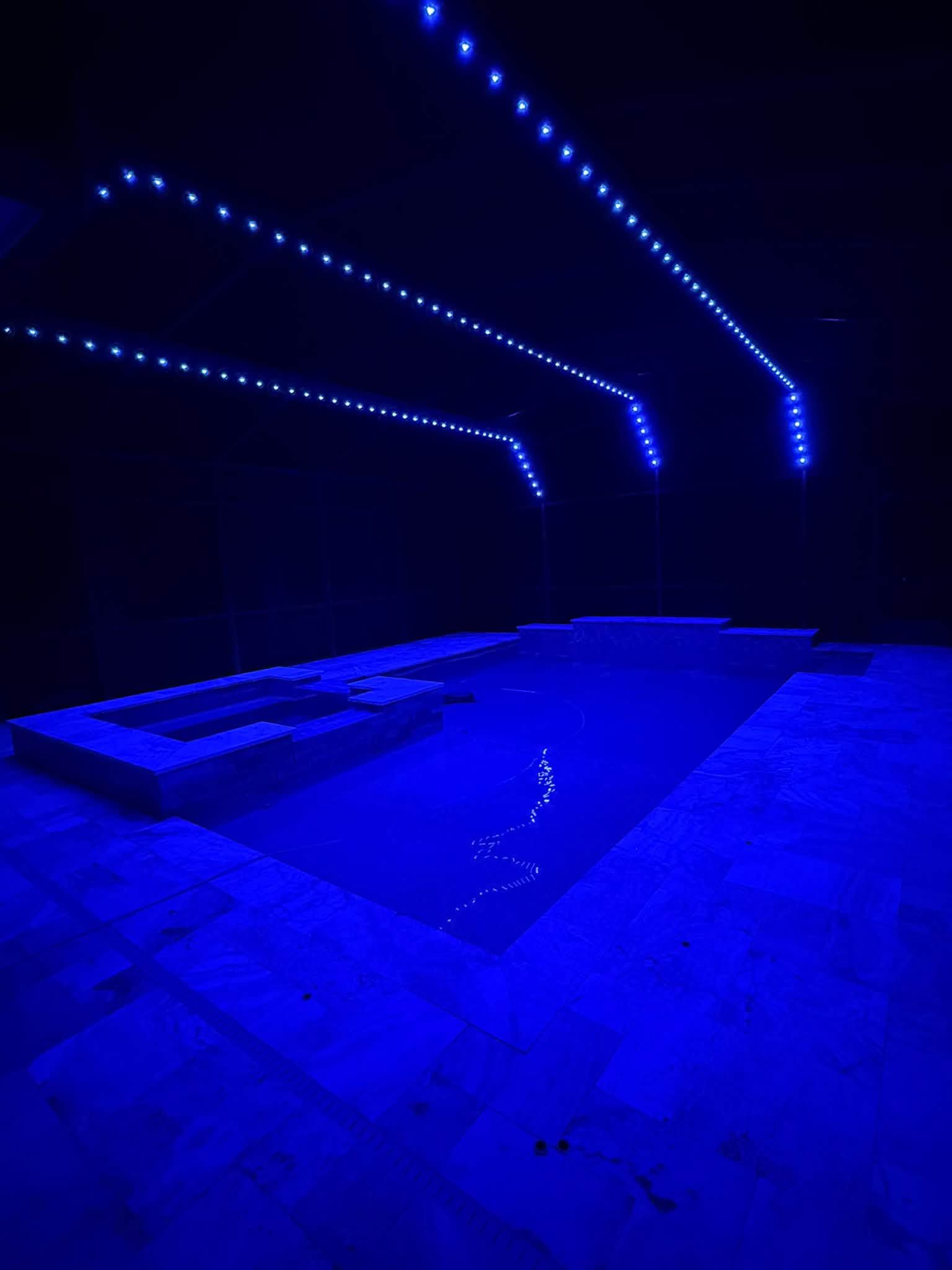 Blue-lit pool area with a swimming pool and glowing overhead lights in a dark indoor space