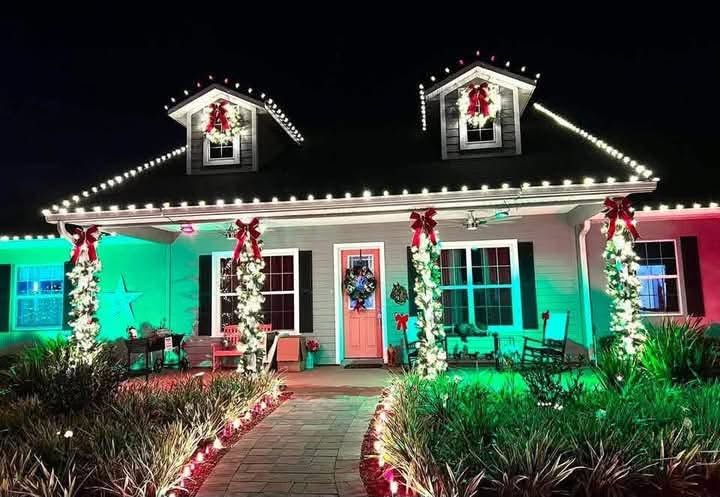 House decorated with colorful Christmas lights and wreaths at night, with a lit walkway leading to the door