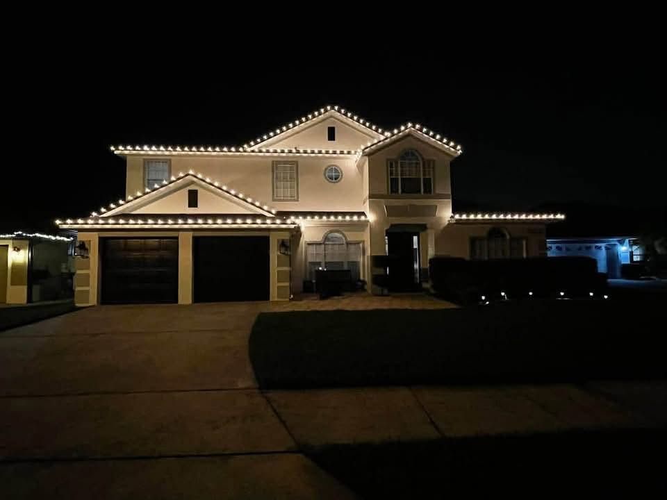 Two-story house at night outlined with white holiday lights, viewed from the driveway.