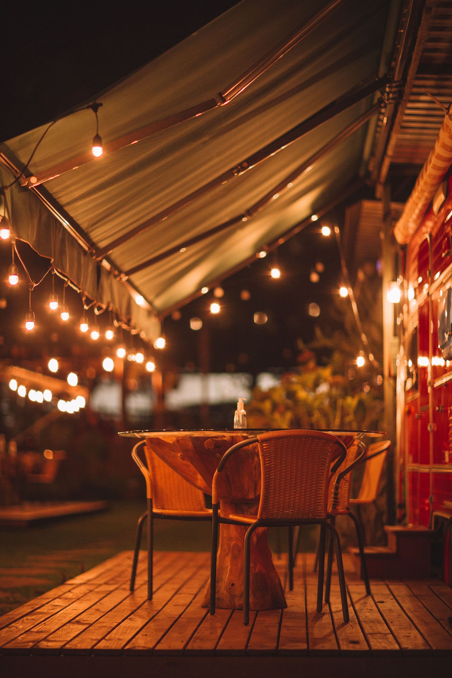 Cozy outdoor café patio with wicker chairs, a table, and warm string lights at dusk