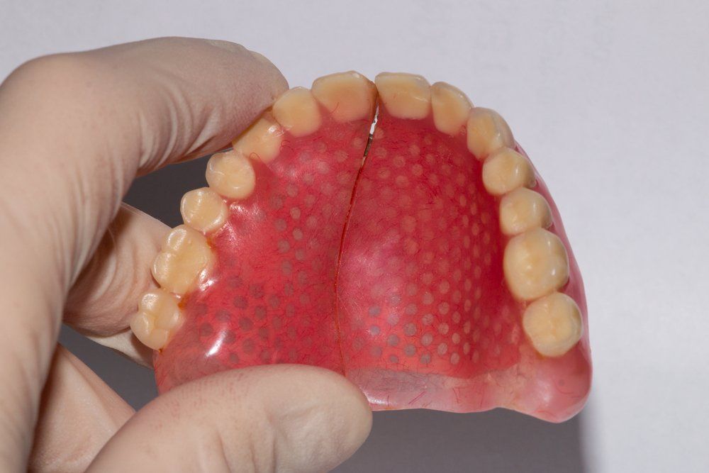 A close-up of a hand holding a removable upper denture with artificial teeth and a pink acrylic base